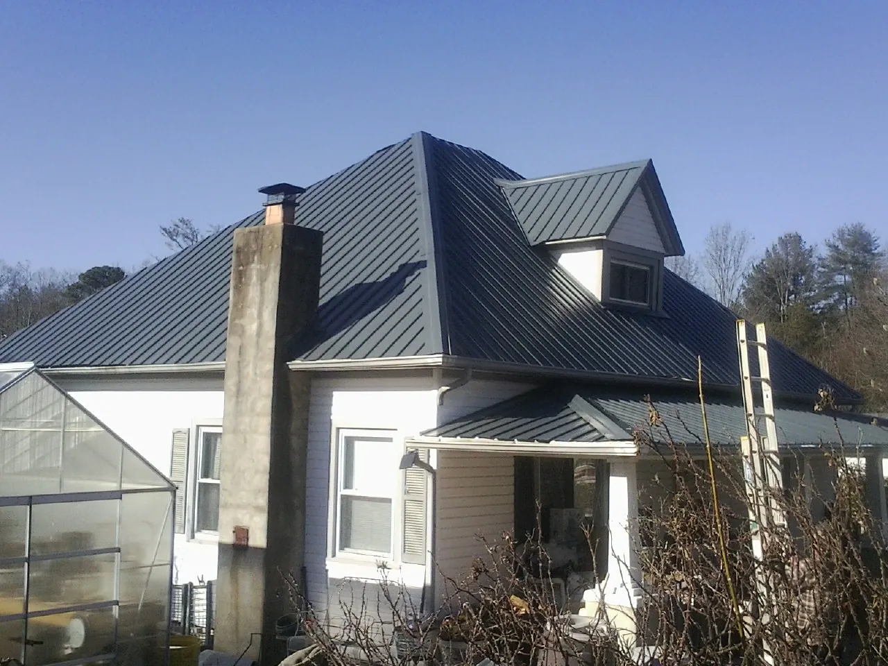 Dark blue standing seam metal roof on a white farmhouse with dormer — Slate & Tile Roof Repair by Roofing Brothers in Hometown
