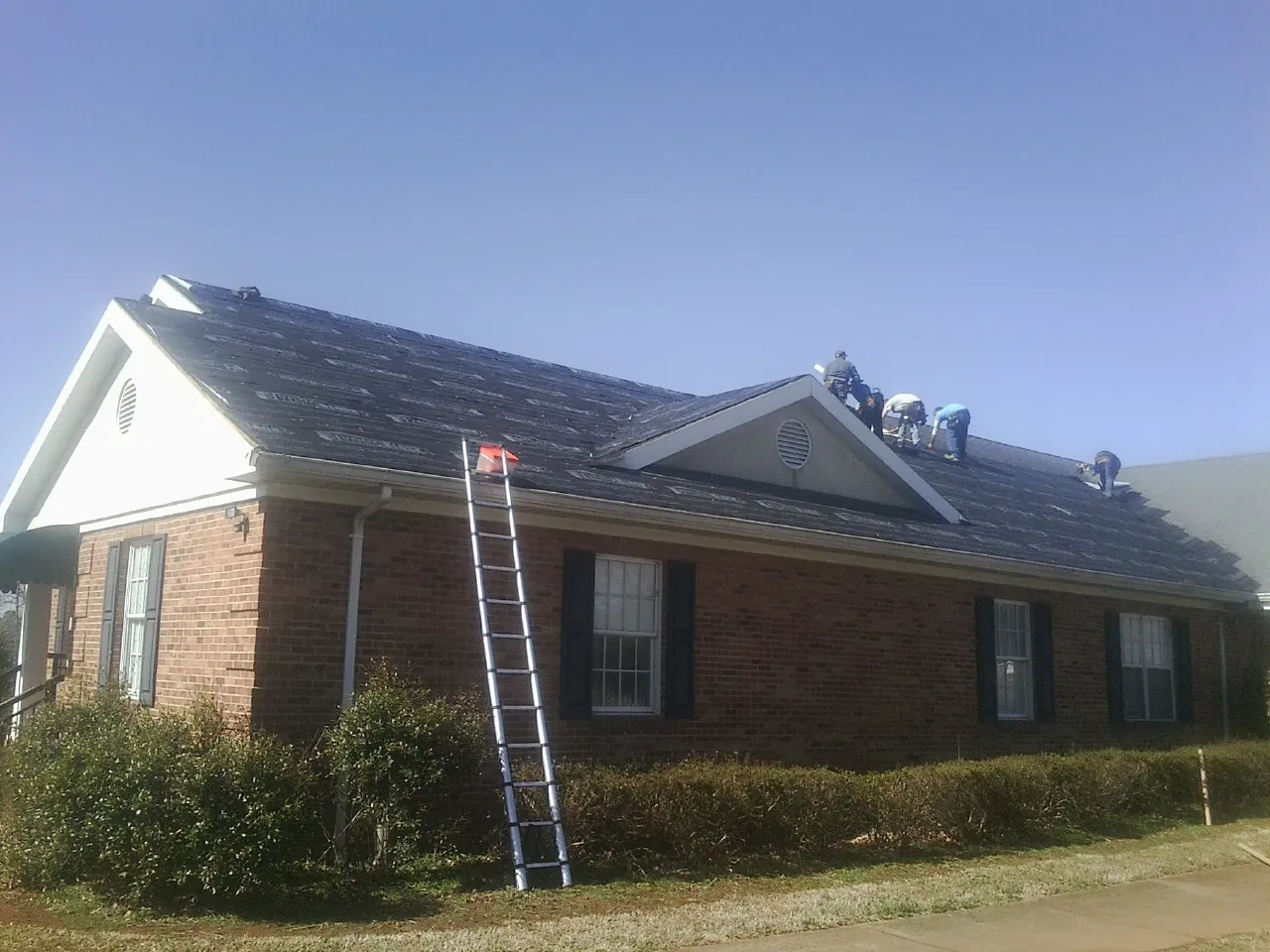 Crew tearing shingles off a brick ranch roof with a ladder set — Emergency Roof Repair work by our crew in Hometown