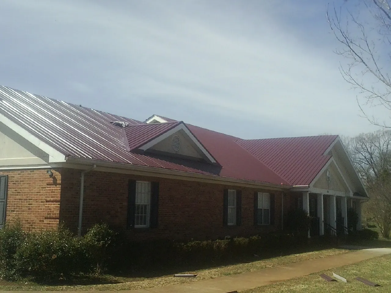 Red metal roof with gabled entries on a long brick building, from a Hail Damage Roof Repair job in Hometown