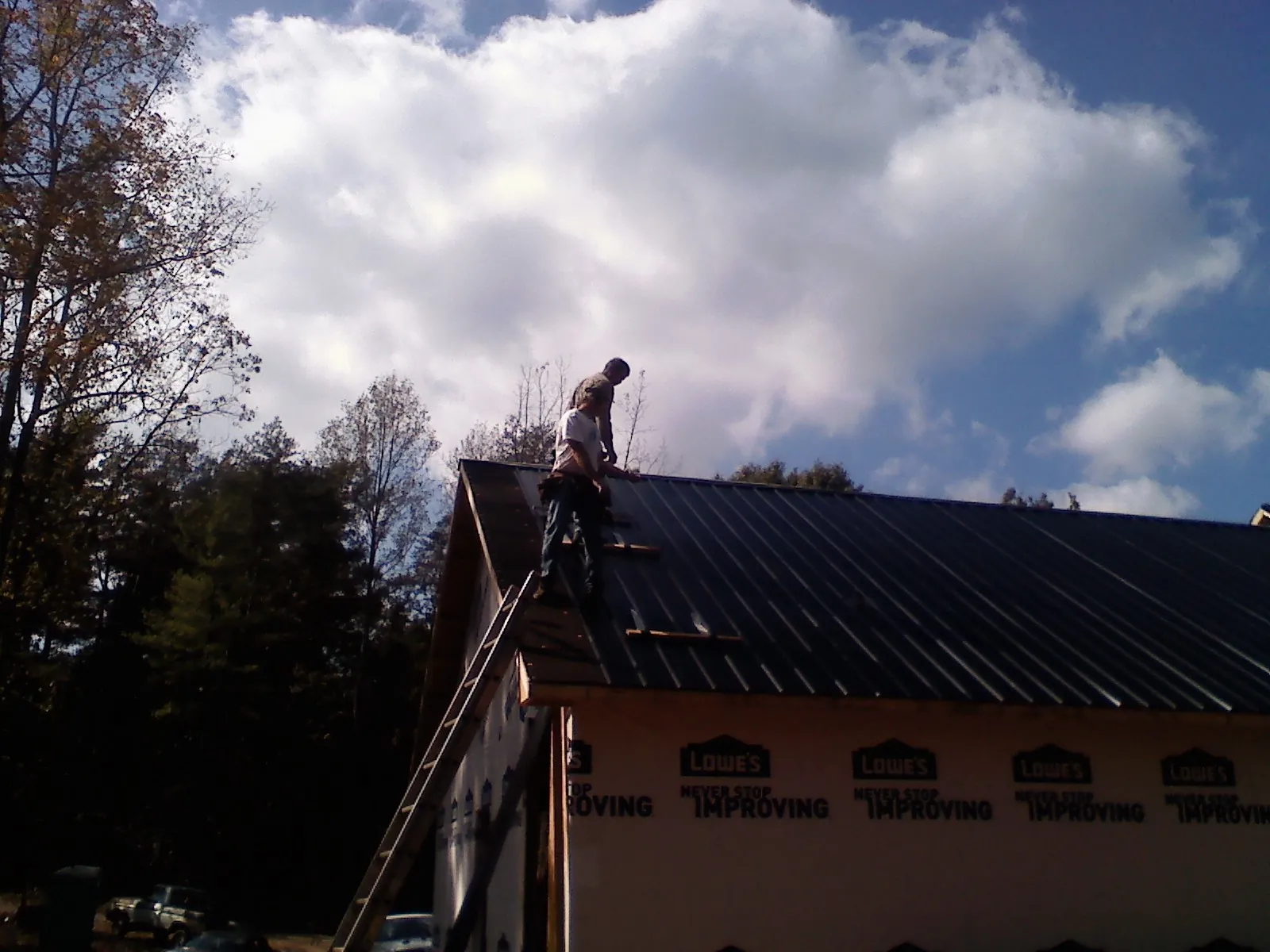 Roofer fastening dark metal panels high against a cloudy sky, from a Roof Inspection job in Hometown