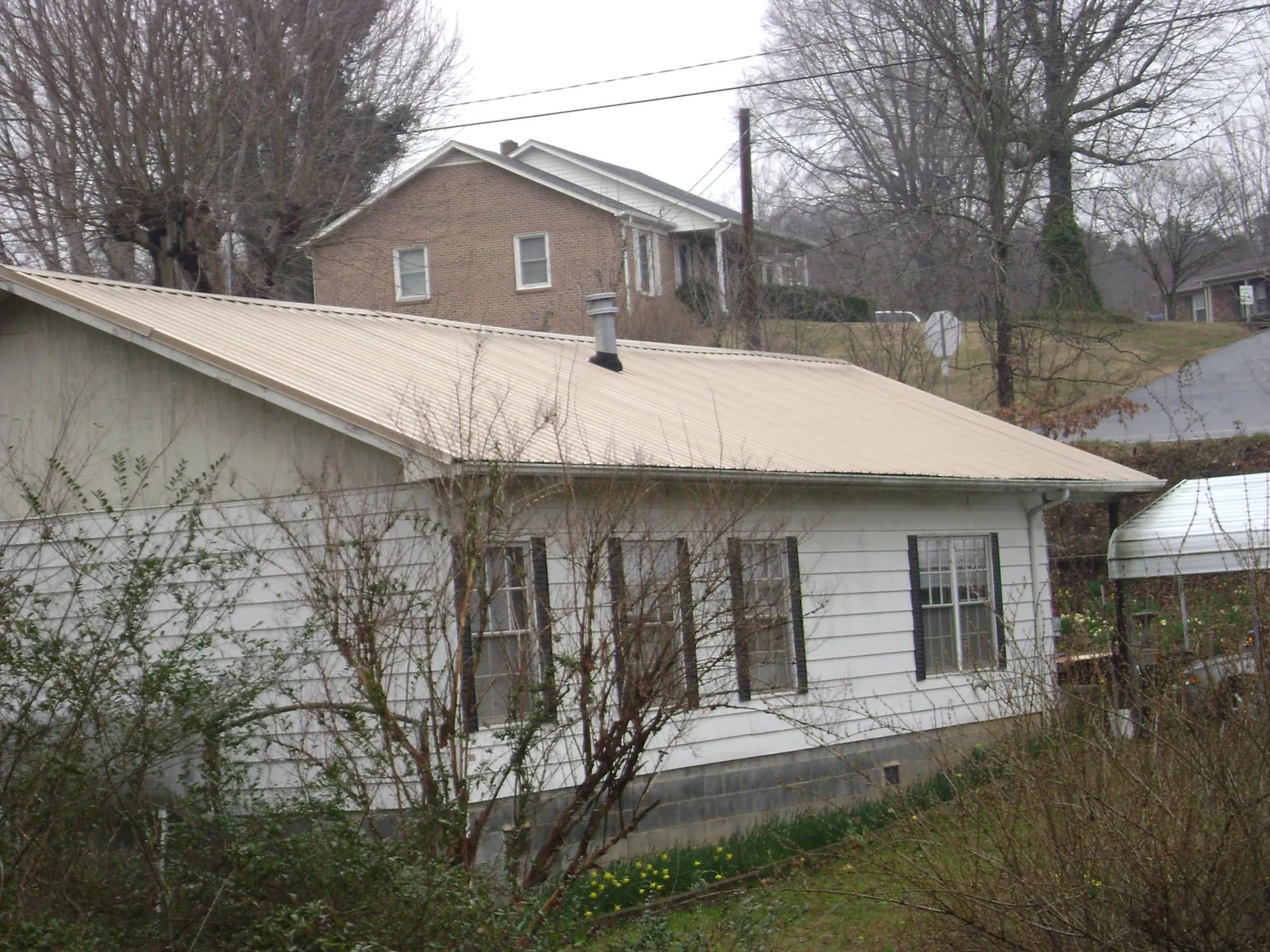 Tan metal roof on a white sided house set into a hillside — Commercial Roofing by Roofing Brothers in Hometown