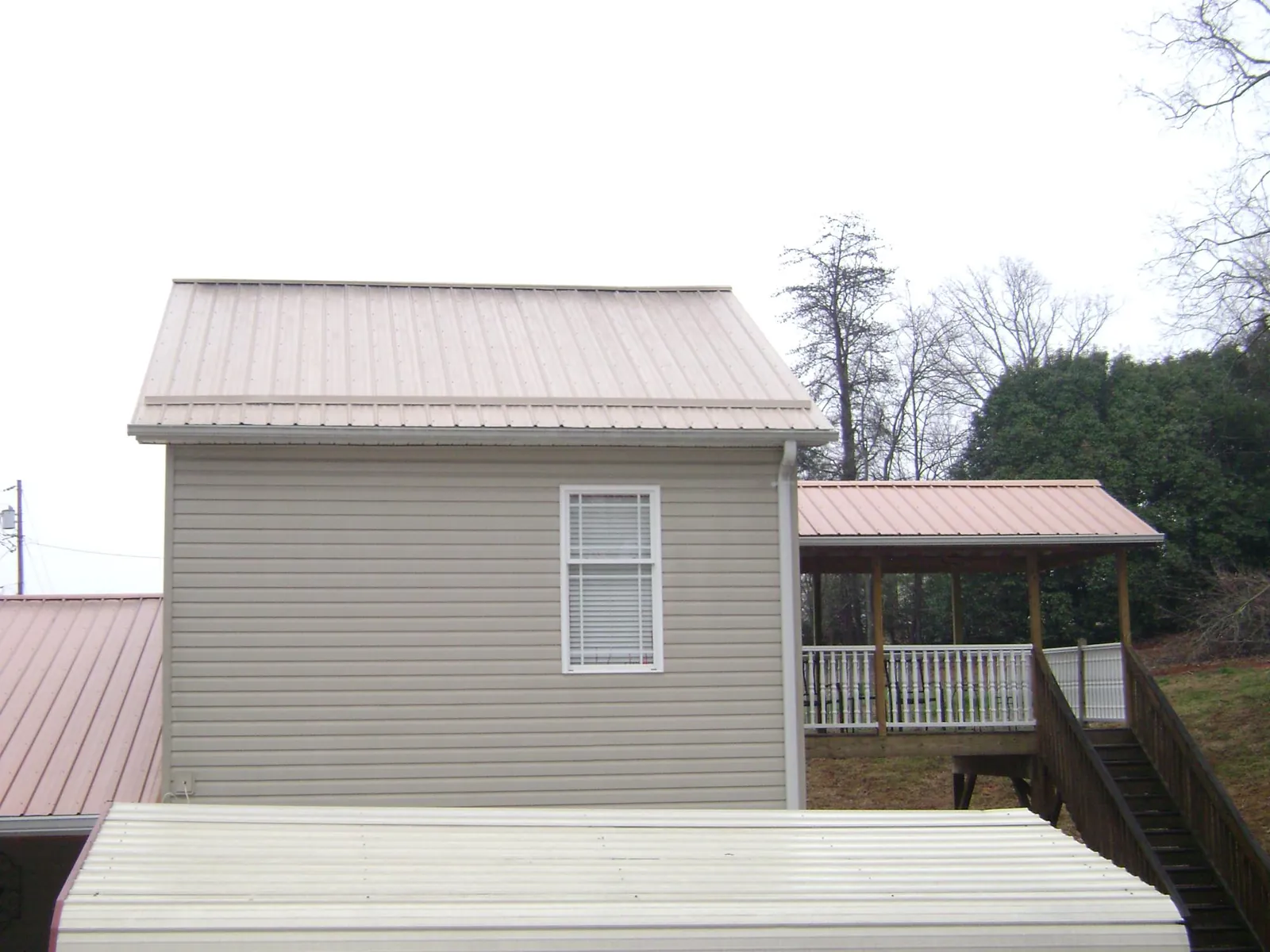 Tan metal roofs on a two story addition and attached porch, from a Roof Replacement job in Hometown